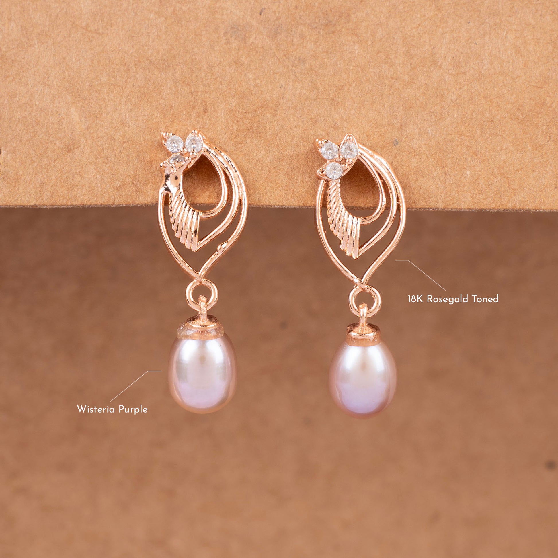 Rose gold earrings with pearl drops on a brown background