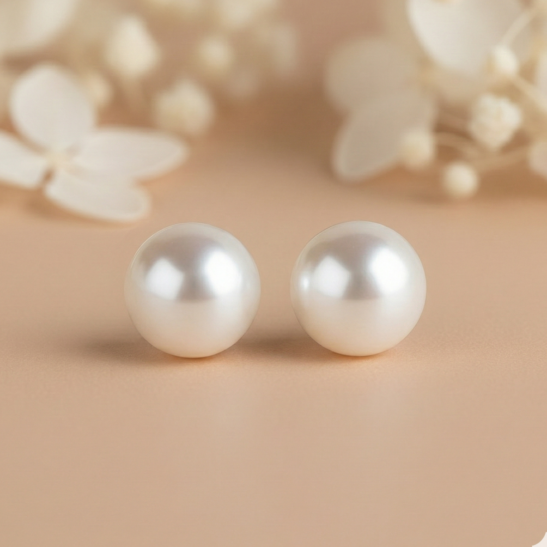 Pair of pearl earrings on a beige background with blurred floral elements