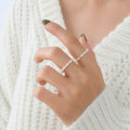 A close-up of a person's hand wearing a delicate double-strand pearl ring, styled with a white knit sweater.