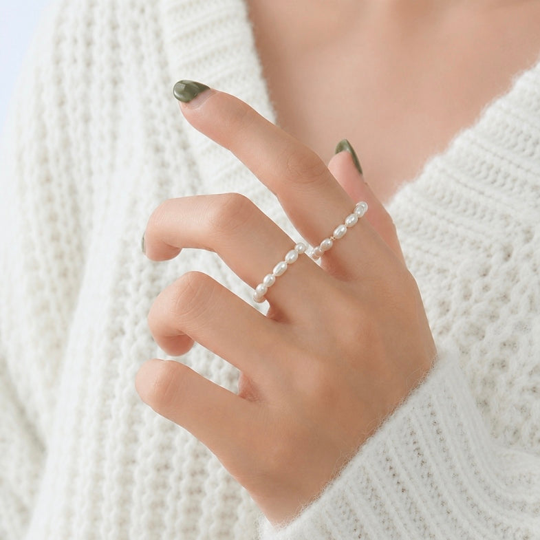 A close-up of a person's hand wearing a delicate double-strand pearl ring, styled with a white knit sweater.