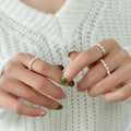 Close-up of a person's hands wearing three delicate pearl rings, styled with green nail polish and a white knit sweater.