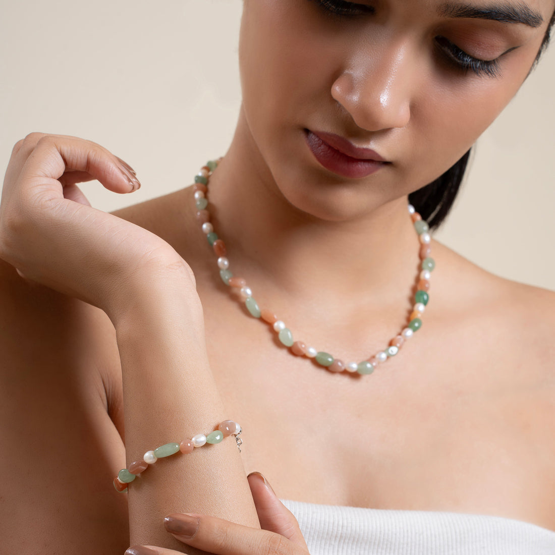 Woman wearing a pearl necklace and bracelet against a neutral background