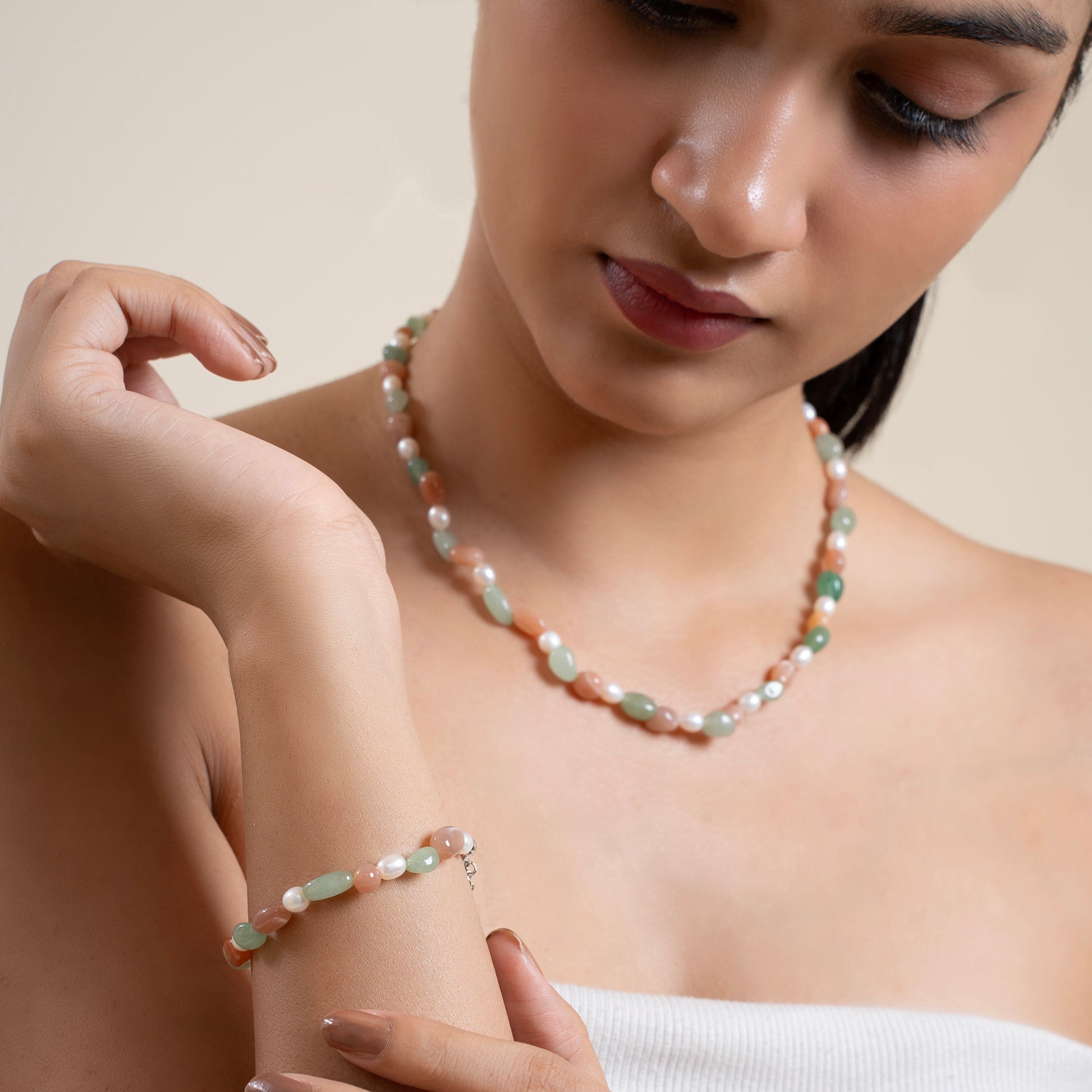 Woman wearing a pearl necklace and bracelet against a neutral background