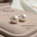 Pearl earrings with silver posts on a soft fabric background, labeled as pure 92.5 silver and real freshwater pearls.