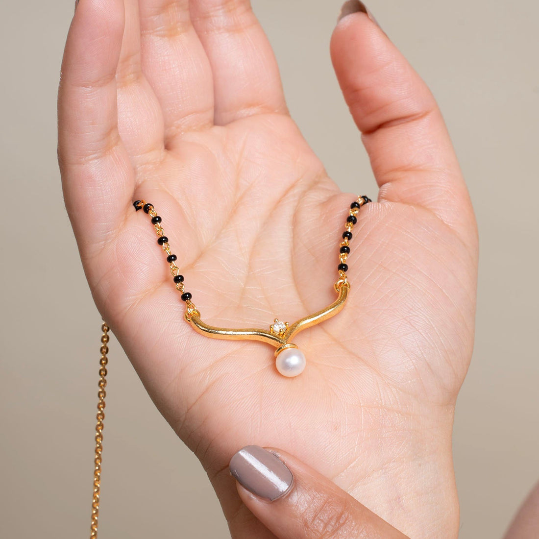 Hand holding a gold bracelet with a pearl on a neutral background