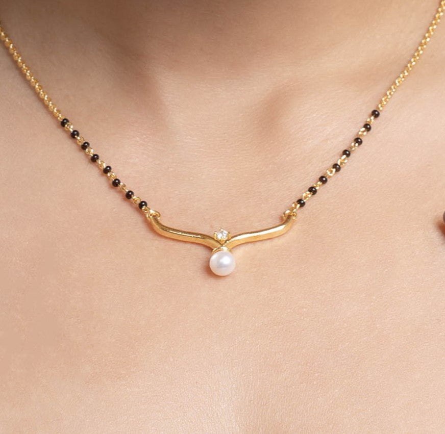Hand holding a gold bracelet with a pearl on a neutral background