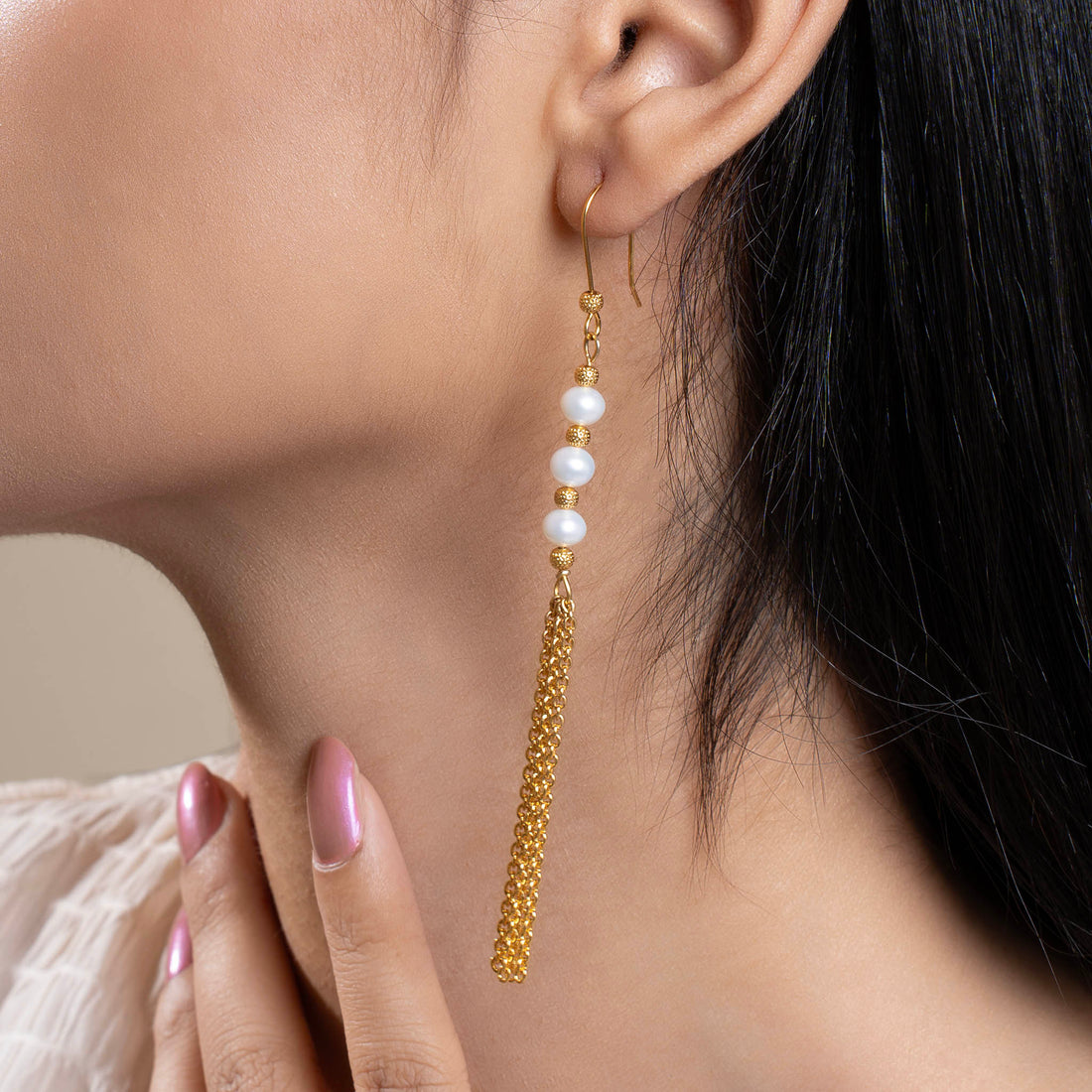 A women wearing a triple pearl tassel earring with gold-colored metal details.