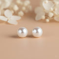 Pearl earrings on a beige background with blurred floral elements