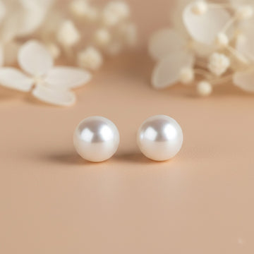 Pearl earrings on a beige background with blurred floral elements